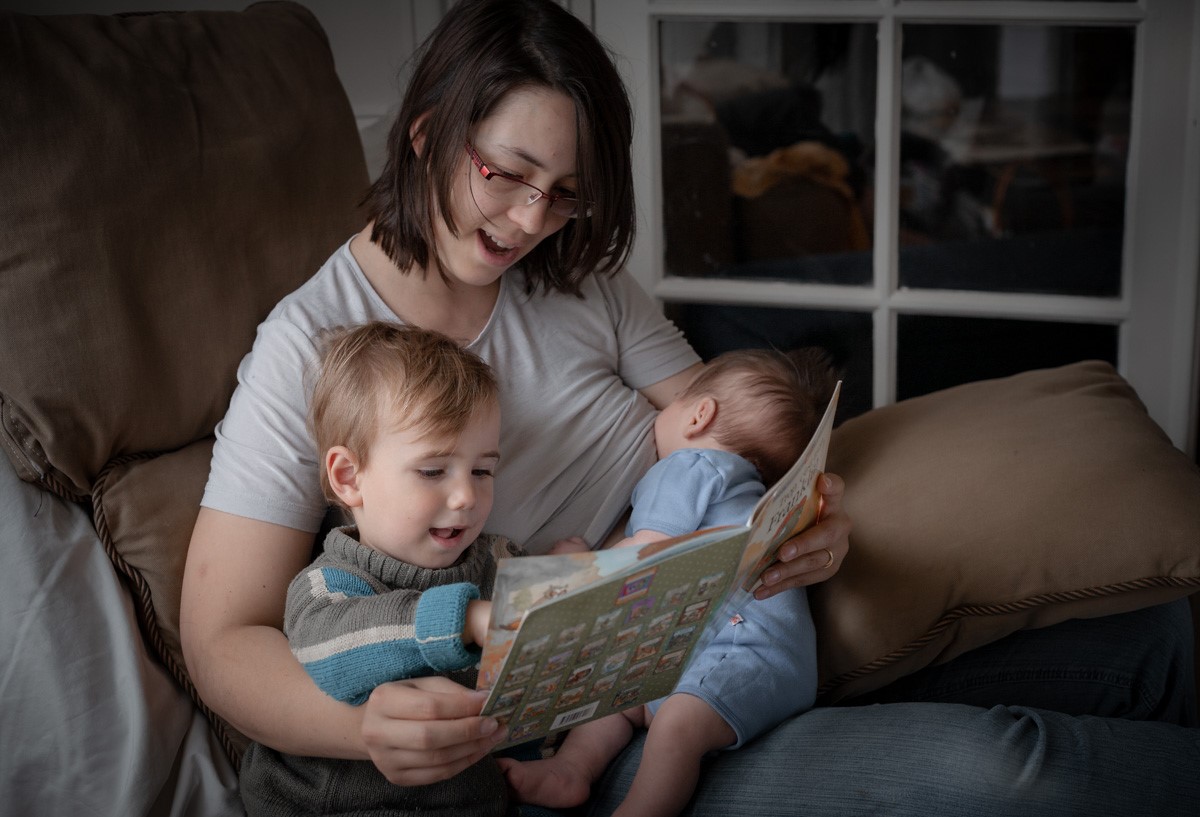 une maman lit un livre à son jeune fils en allaitant son bébé